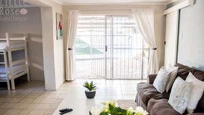 A room with a brown sofa, a white coffee table, a potted plant, and a bunk bed. - Little Rose Guesthouse & Self-Catering (Gqeberha (Port Elizabeth))