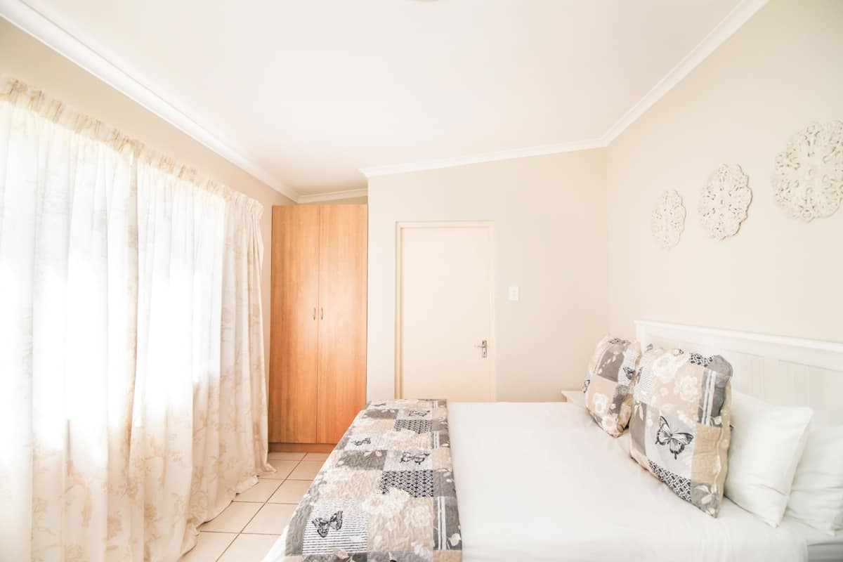 A bedroom with a bed, a wooden door, and a window with curtains.