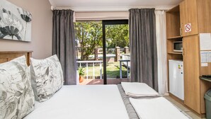 A hotel room with a bed, a wooden wardrobe, a small fridge, and a balcony with curtains. - Little Rose Guesthouse & Self-Catering (Gqeberha (Port Elizabeth))