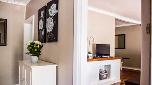 A hallway with a white console table, a potted plant, and two black and white rose paintings on the wall. - Little Rose Guesthouse & Self-Catering (Gqeberha (Port Elizabeth))