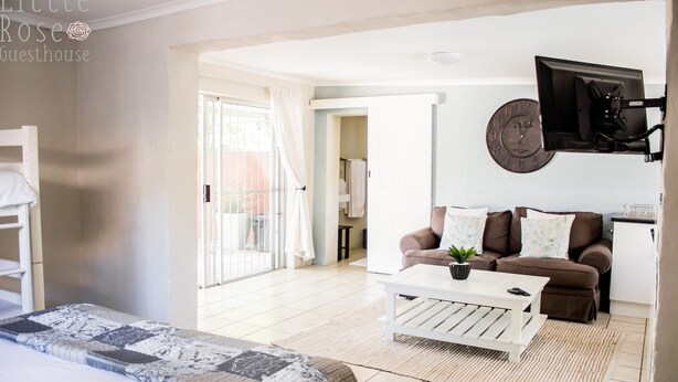 A modern guest room with a bed, a white coffee table, a brown sofa, and a TV mounted on the wall. - Little Rose Guesthouse & Self-Catering (Gqeberha (Port Elizabeth))