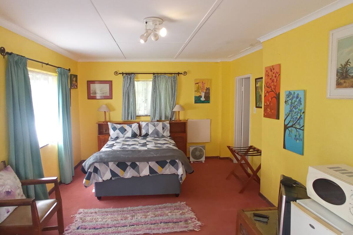 Quarto com cama, escrivaninha, cadeira, ventoinha e micro-ondas.