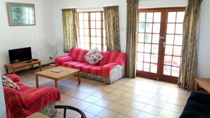 Una sala de estar con sofá, mesa de centro, televisor y ventana con cortinas.