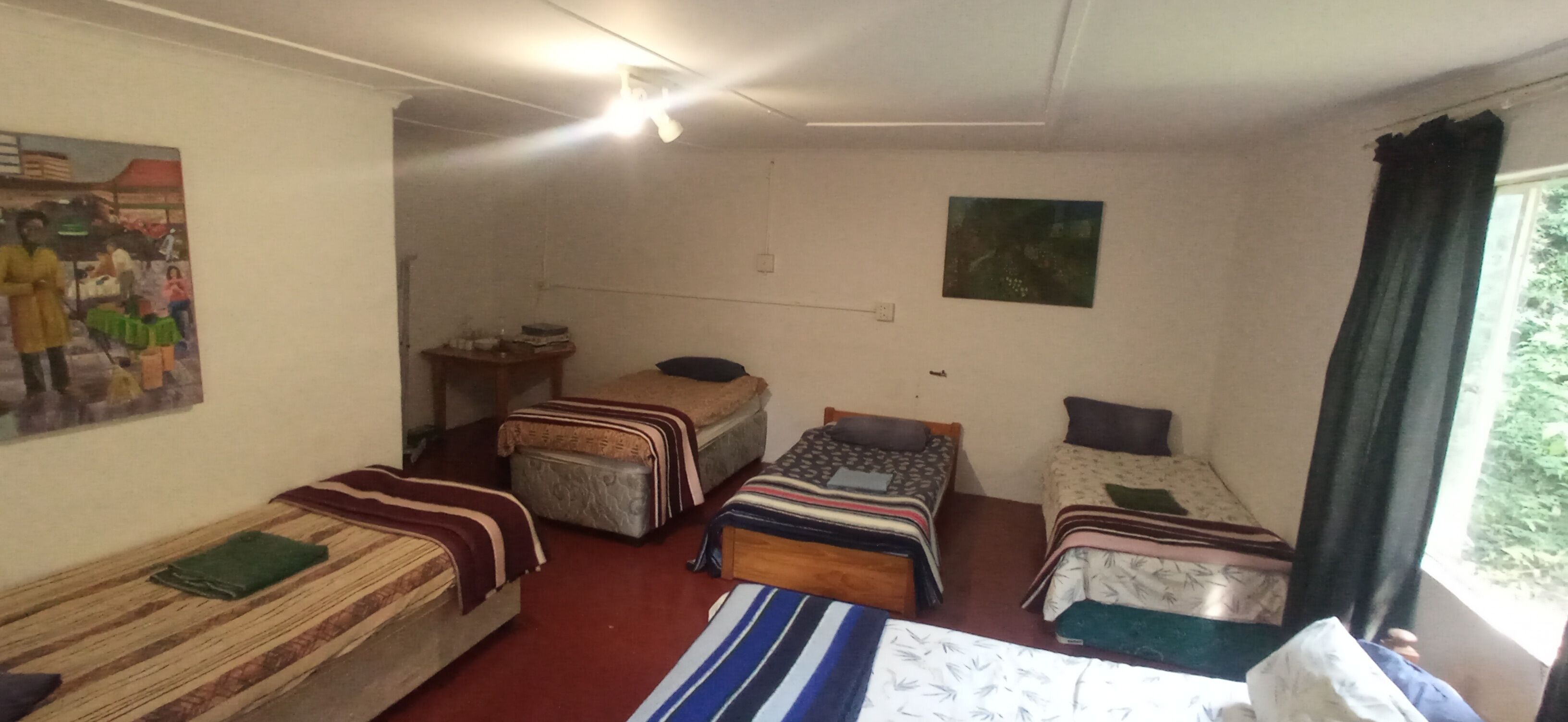 Een studentenkamer met twee eenpersoonsbedden, een klein tafeltje, een stoel en een wandplank.