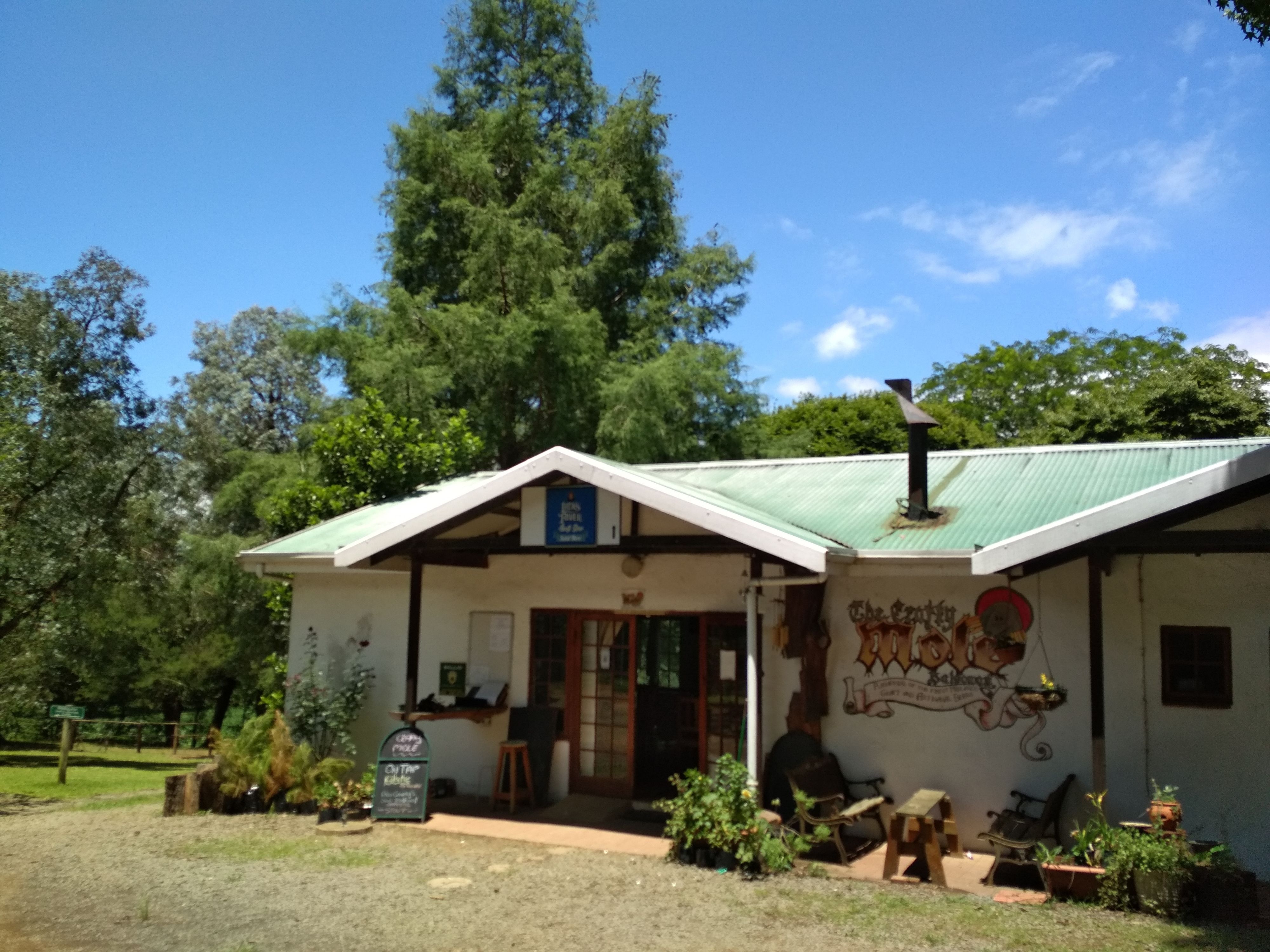 Un edificio pequeño con techo verde, un letrero que dice "The Country Kitchen" y mesas con sillas para sentarse al aire libre.