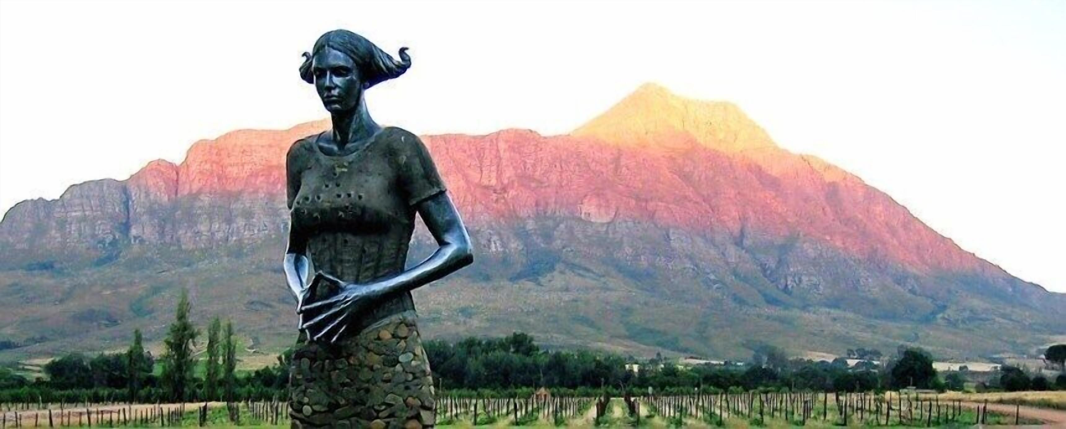 A statue of a woman in a dress with a mountainous background.