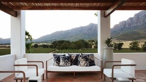 A terrace with white sofas and chairs, a wooden pergola, and a view of mountains and fields. - Fraaigelegen Farm (Tulbagh)
