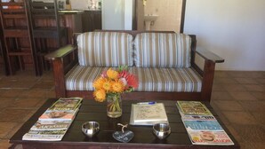 A living room with a sofa, a coffee table with magazines, bowls, and a vase with flowers. - Fraaigelegen Farm (Tulbagh)