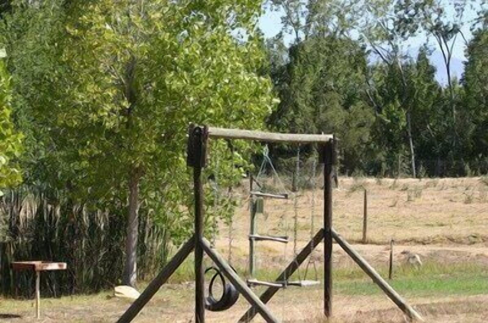 A playground with a swing set and tire swing in a grassy area with trees.
