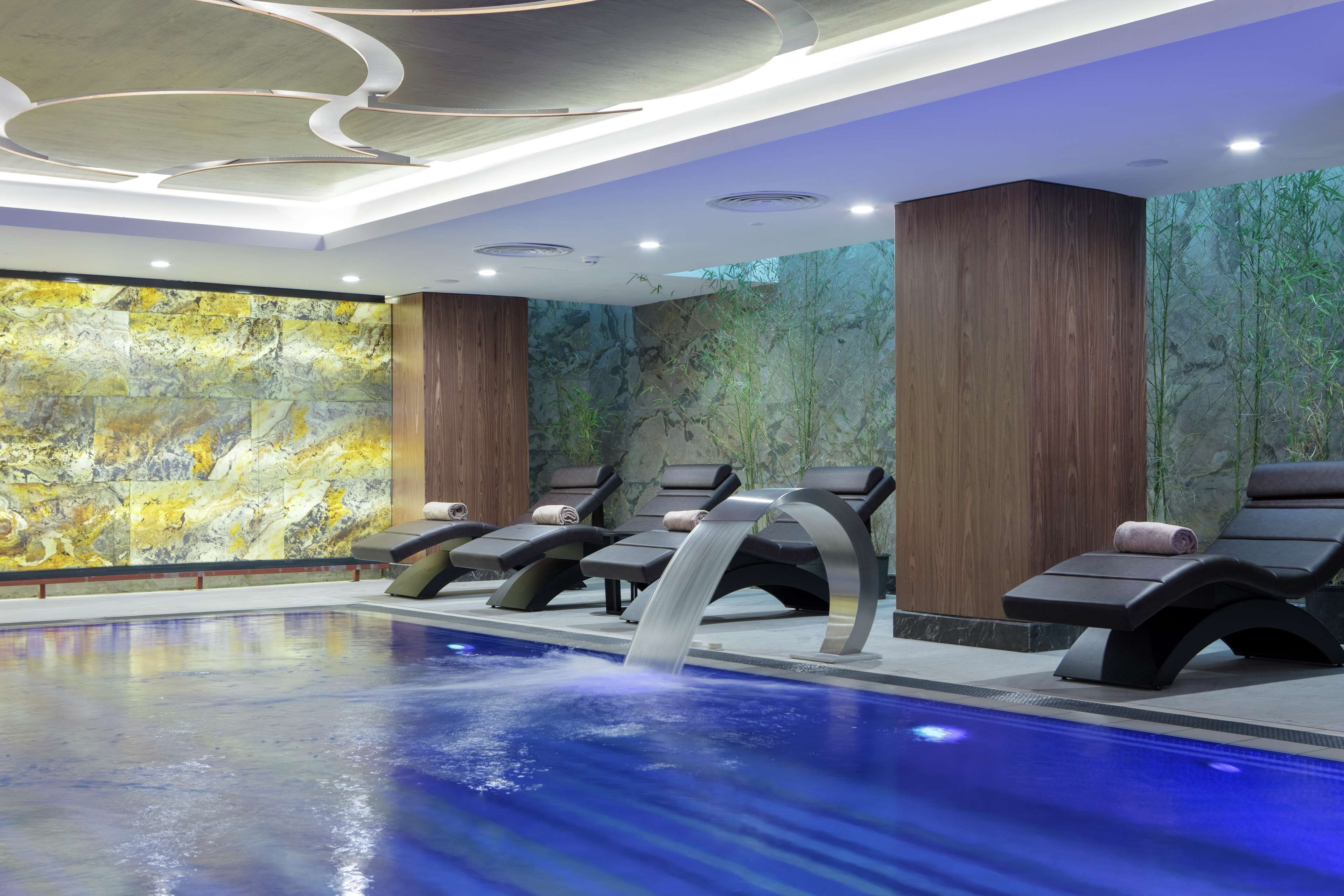 A modern indoor pool area with lounge chairs and a waterfall feature.