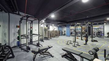 Academia com diversos equipamentos de musculação, bancos e um espelho grande na parede.