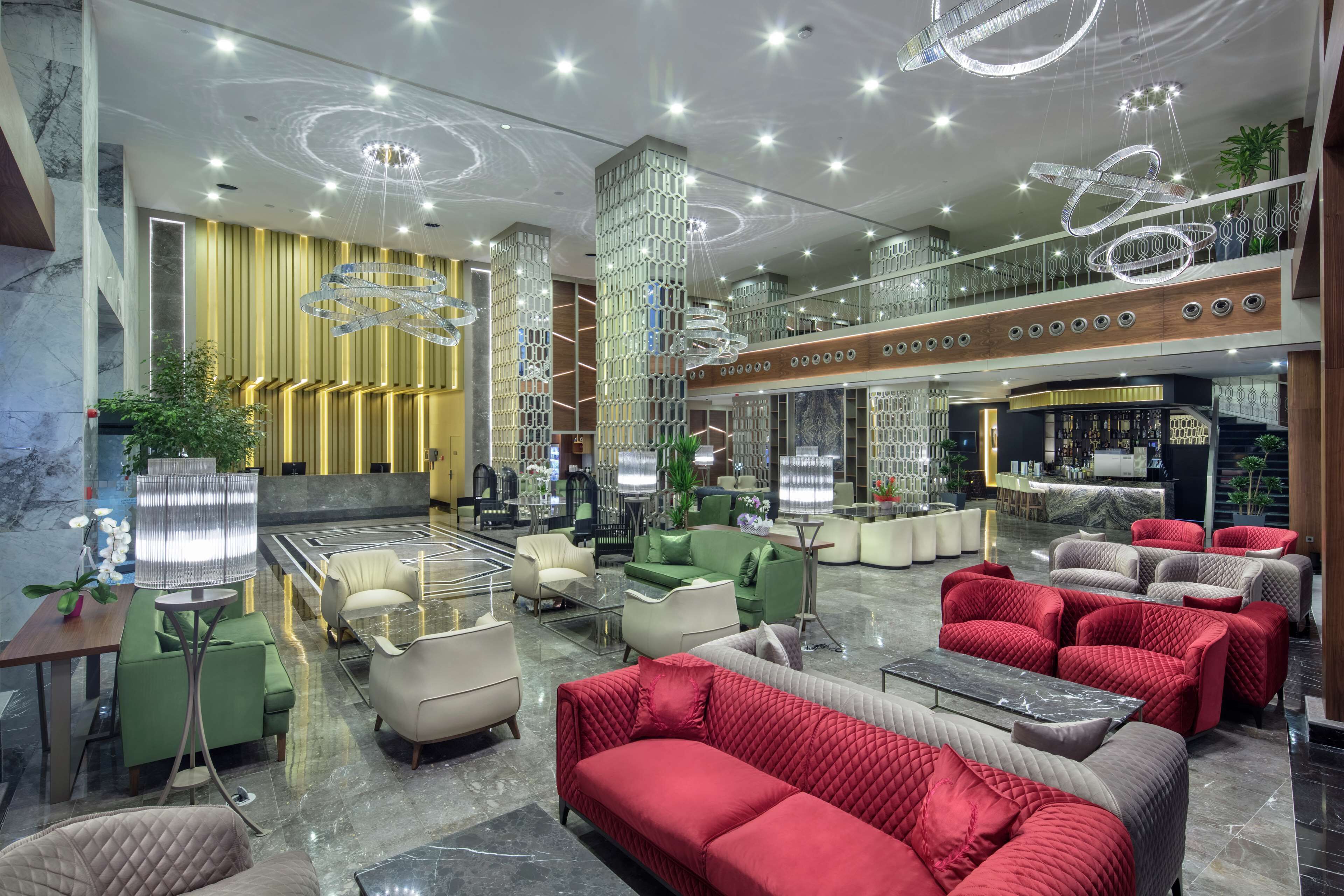A spacious lobby with modern furniture, a bar area, and a high ceiling with decorative lighting.