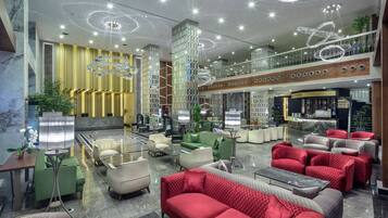 A spacious lobby with modern furniture, a bar area, and a high ceiling with decorative lighting.