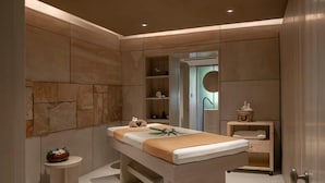Een moderne spa-ruimte met een massagetafel, een klein bijzettafeltje, een plank met toiletartikelen en een stenen muur.