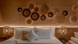 Een hotelkamer met een bed, kussens, een nachtkastje met een lamp en een decoratie aan de muur.