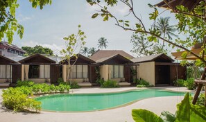 A pool area with multiple bungalow-style accommodations, surrounded by greenery and palm trees.