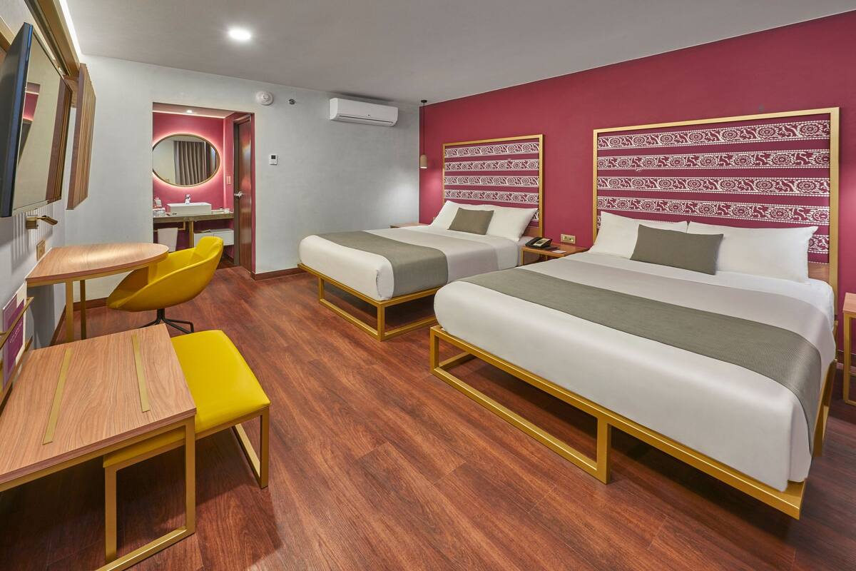 A hotel room with two beds, a desk, a chair, and a vanity with a mirror.