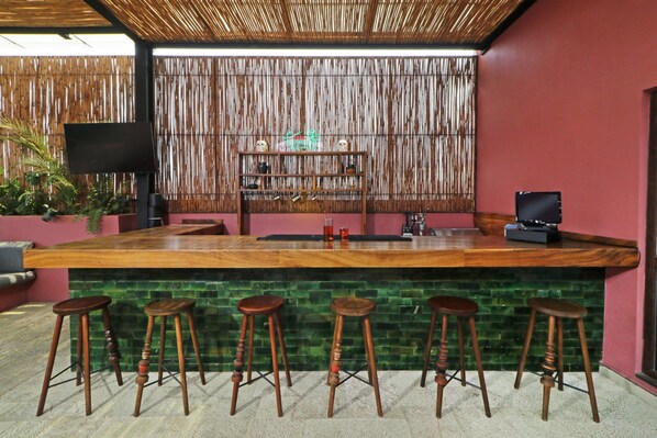 A bar area with a wooden counter, green mosaic tiles, and wooden stools.