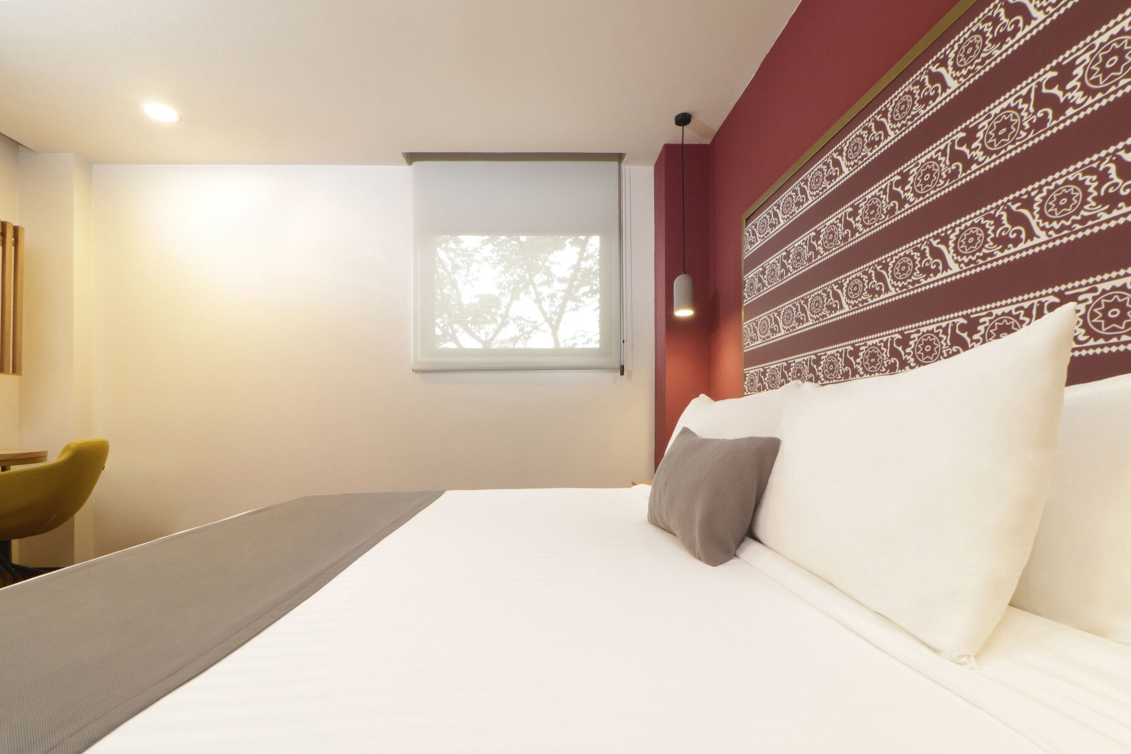 A modern hotel room with a large bed, a small window, and a decorative wall pattern.