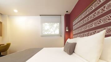 A modern hotel room with a large bed, a small window, and a decorative wall pattern.