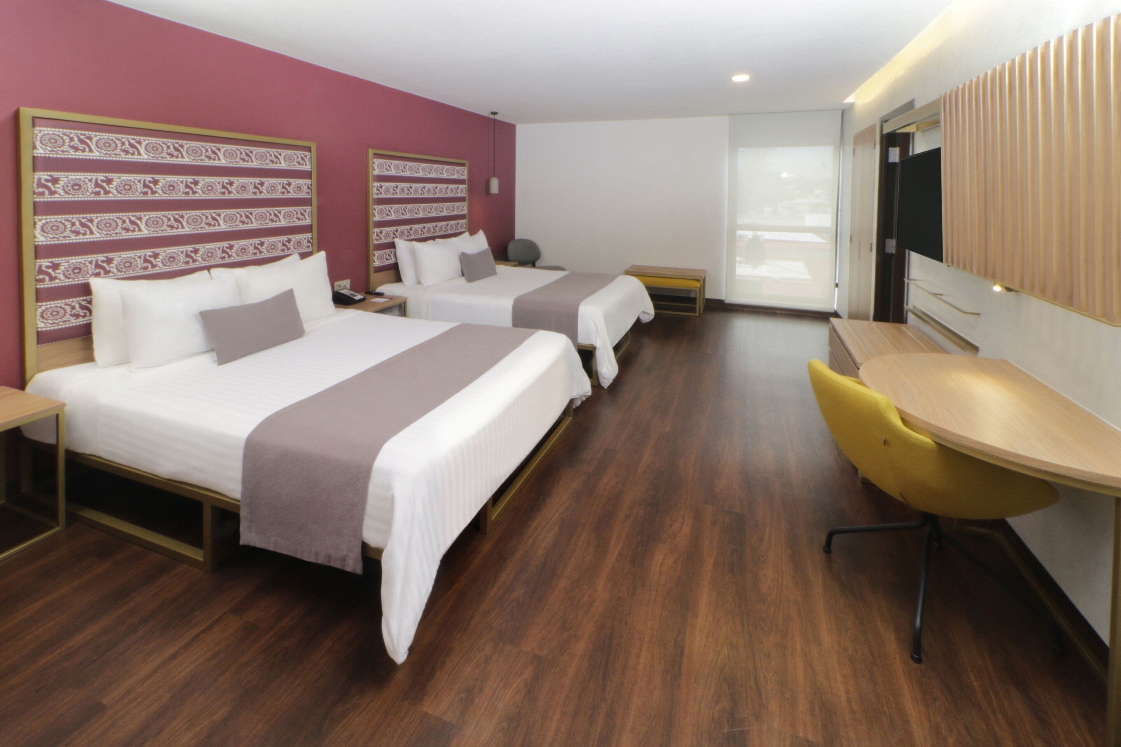 A hotel room with two beds, a desk, and a chair.