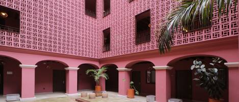 A courtyard with a patterned pink wall, arches, and potted plants.