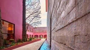 A narrow pathway with a blue water feature, flanked by a pink building and a wooden wall. - City Centro by Marriott Oaxaca (Oaxaca)