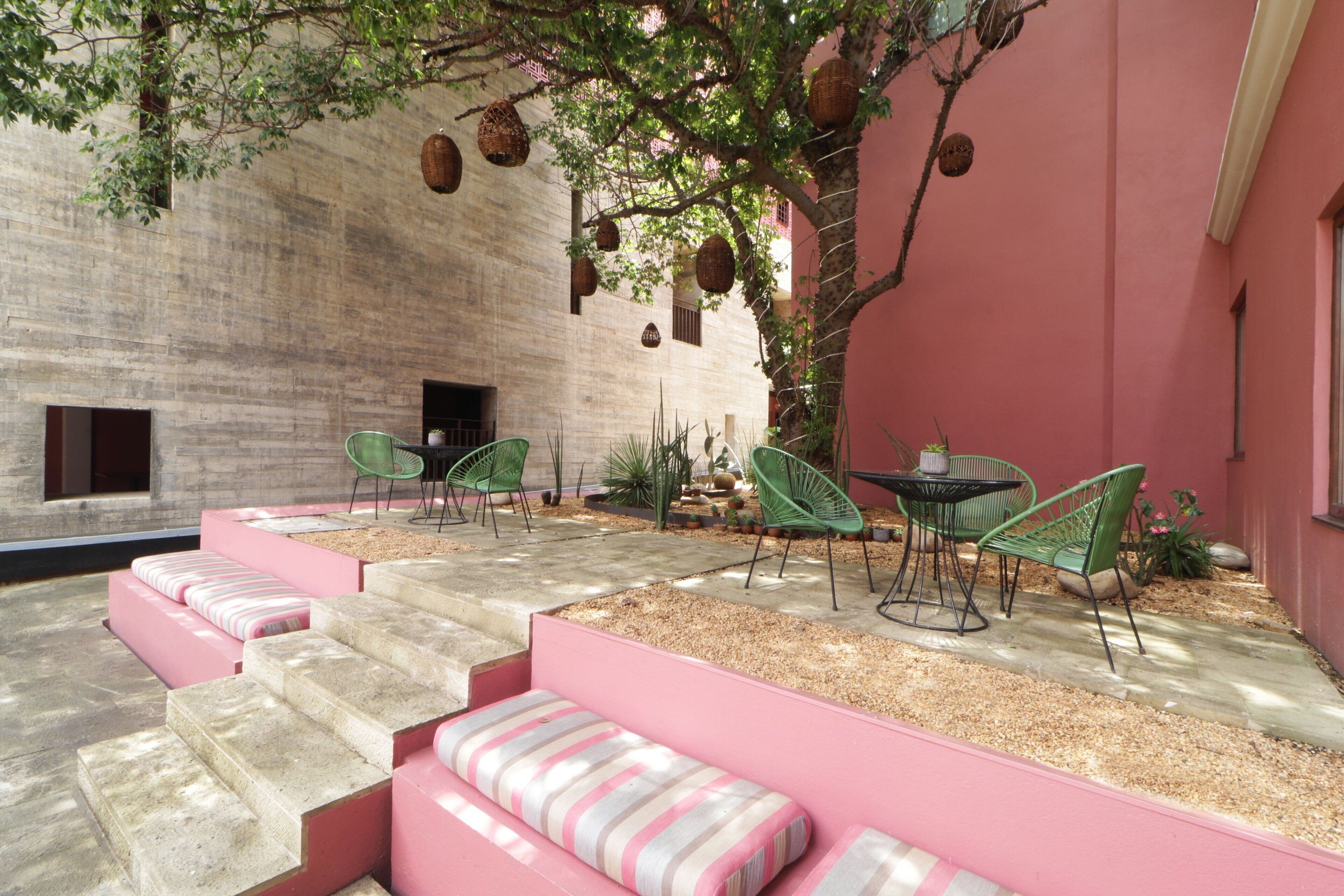 Une cour avec des marches menant à un espace aménagé pour s’asseoir, le tout entouré d’un mur rose et d’un arbre.