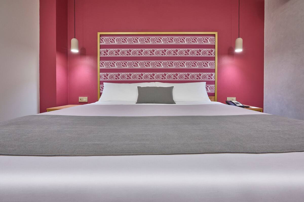 A bed with a patterned headboard, white bedding, and a grey throw.