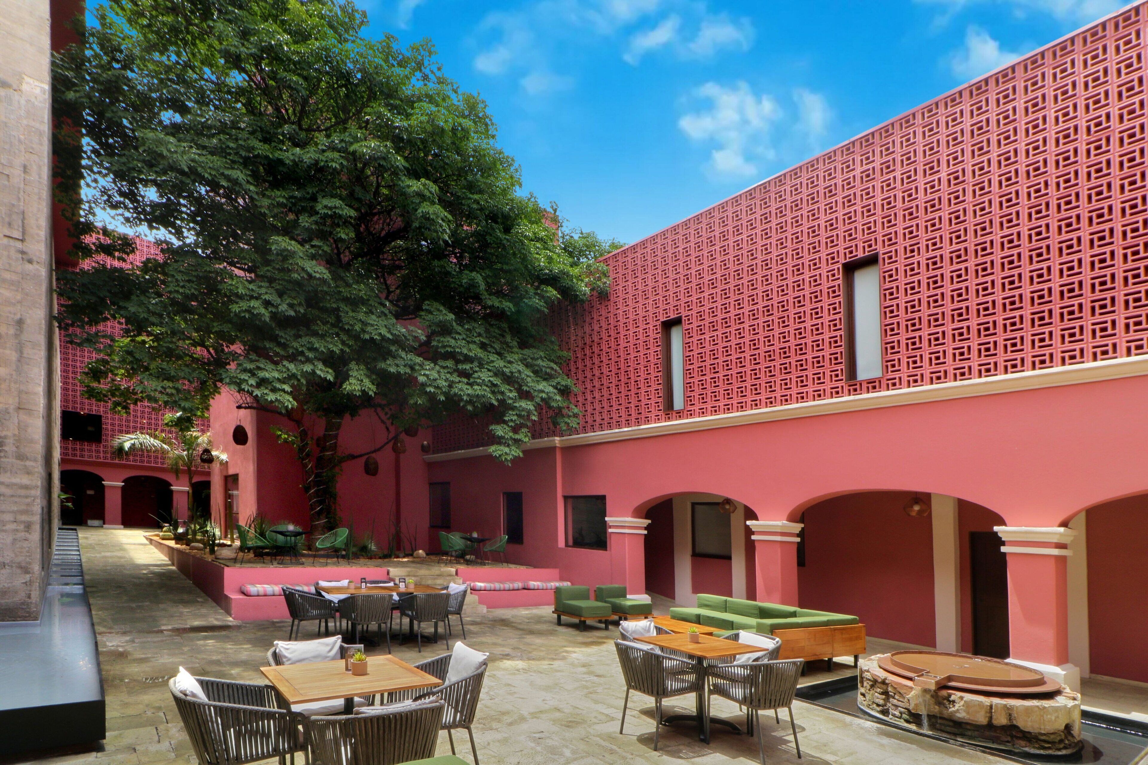 An outdoor courtyard with red brick walls, green seating, and tables arranged for dining.