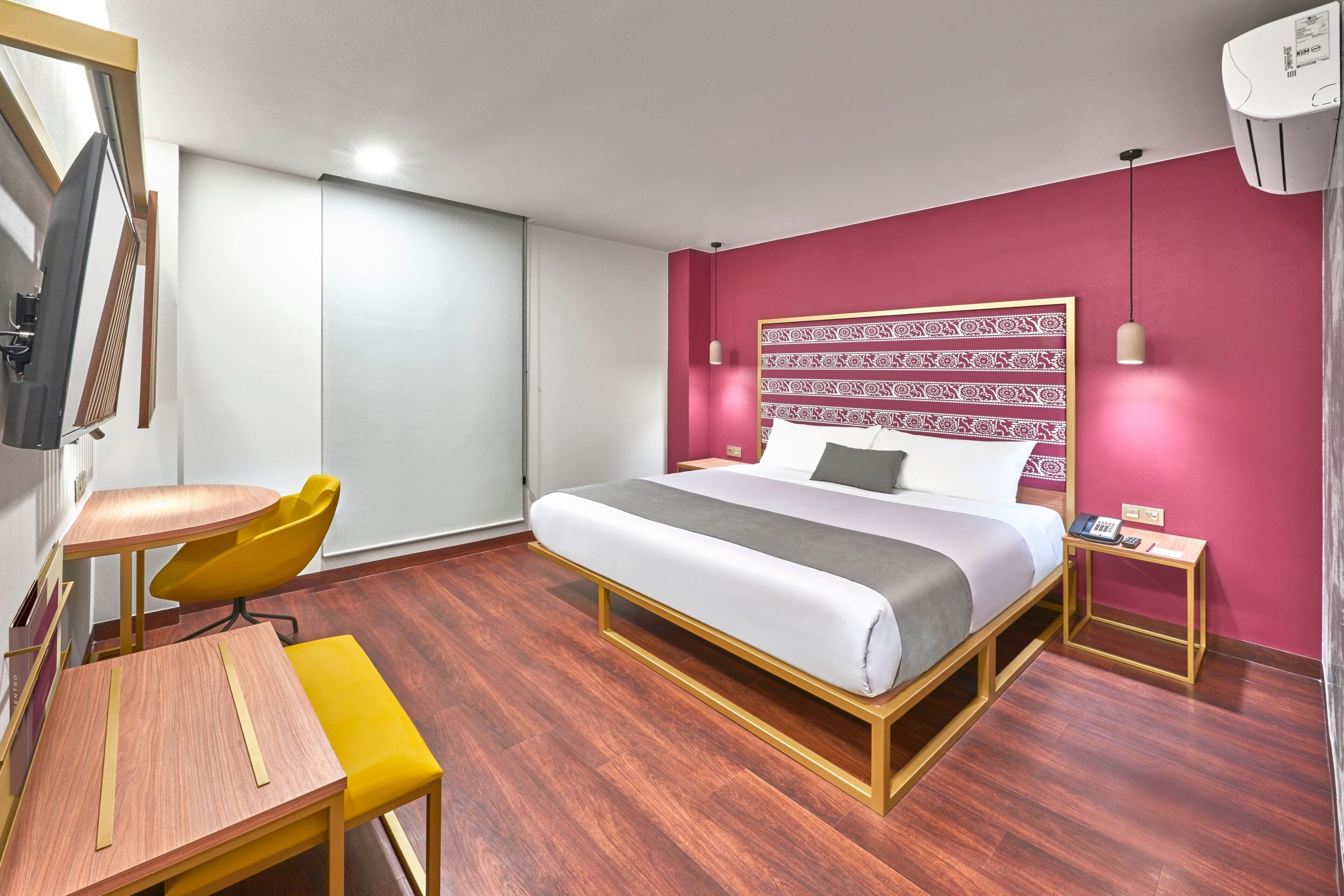 A hotel room with a bed, bedside table, chair, and a desk with a chair.