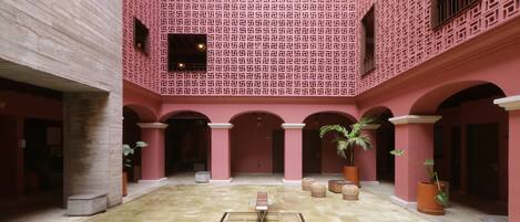 An indoor courtyard with a patterned wall, columns, and potted plants.