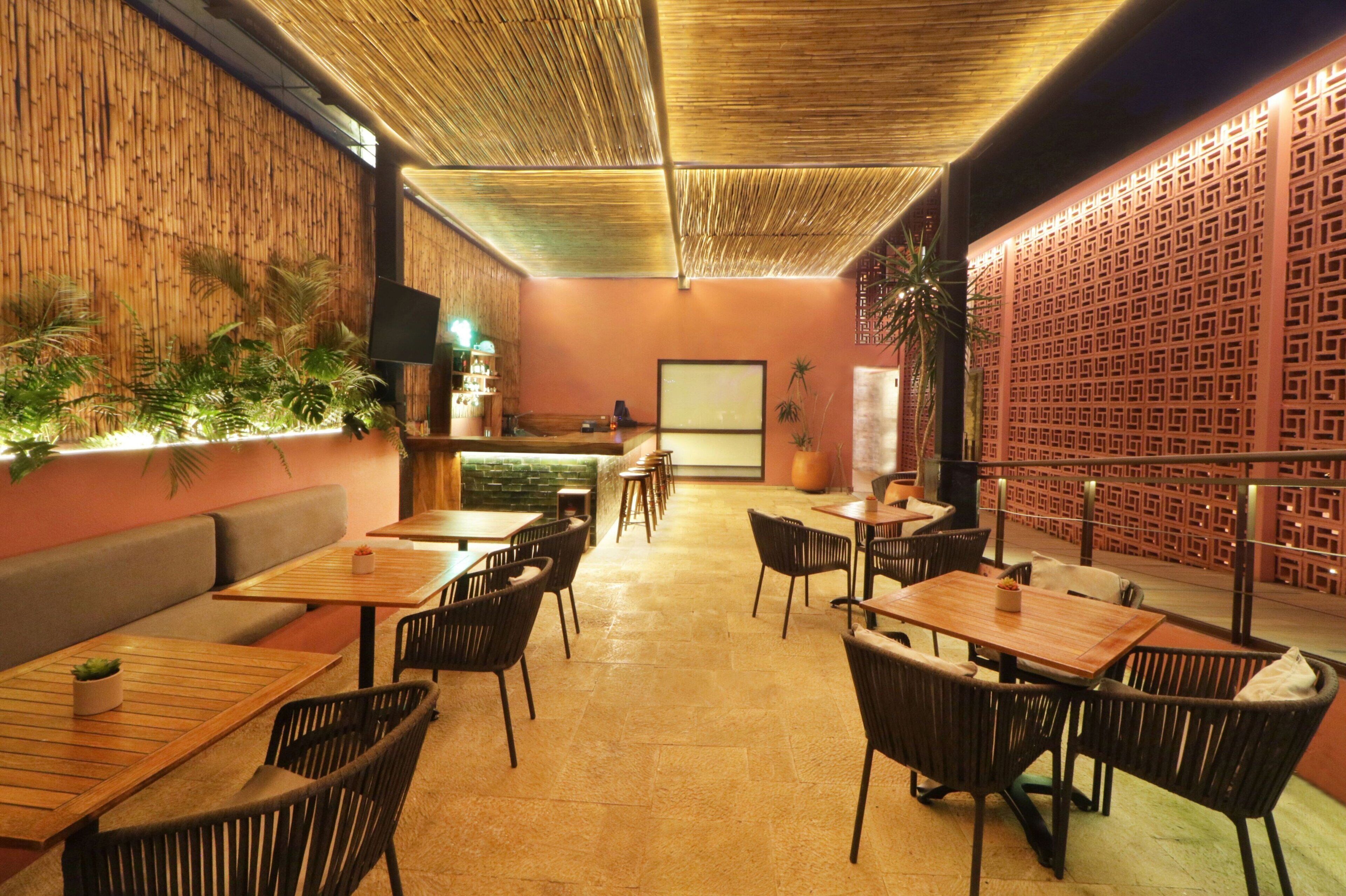 Restaurante com mesas e cadeiras de madeira, um balcão e uma parede decorativa com padrão geométrico.