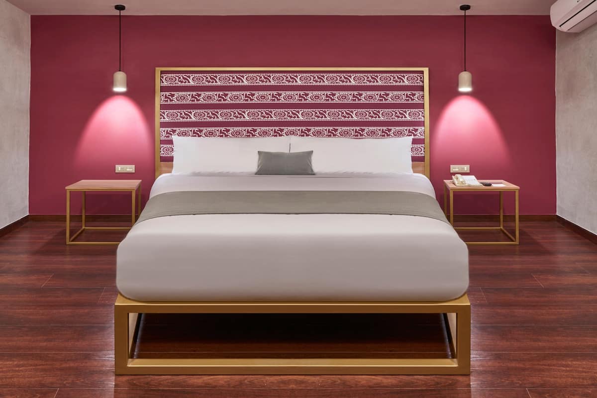 A modern hotel room with a large bed, patterned headboard, bedside tables, and pendant lighting.