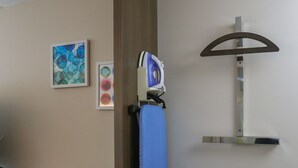 Una habitación de hotel con un banco de madera, una tabla de planchar azul y una estación de planchado fijada a la pared.