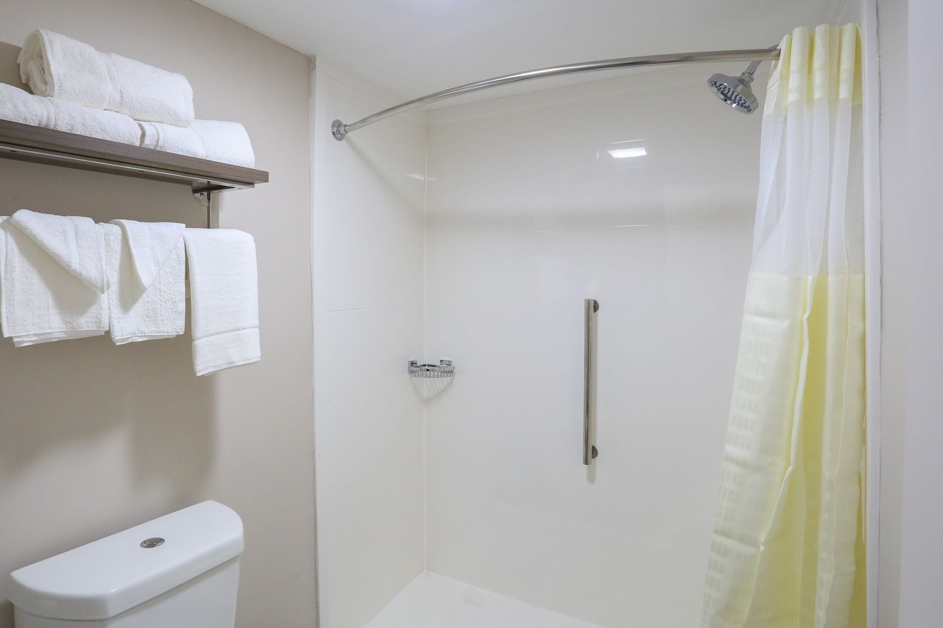 Un petit espace douche fermé, doté d’une porte en verre, de toilettes et d’un porte-serviettes avec des serviettes pliées.