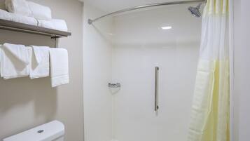 Un petit espace douche fermé, doté d’une porte en verre, de toilettes et d’un porte-serviettes avec des serviettes pliées.