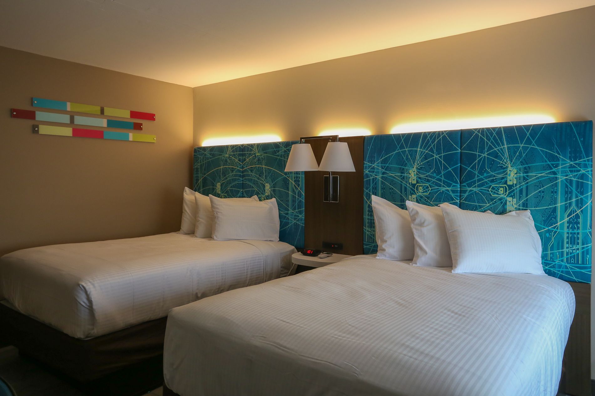 A hotel room with two beds, a wall art piece, and a modern headboard.
