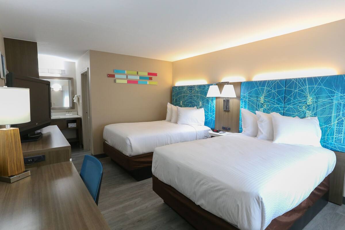 A hotel room with two beds, a desk with a lamp, a TV, and a mirror.
