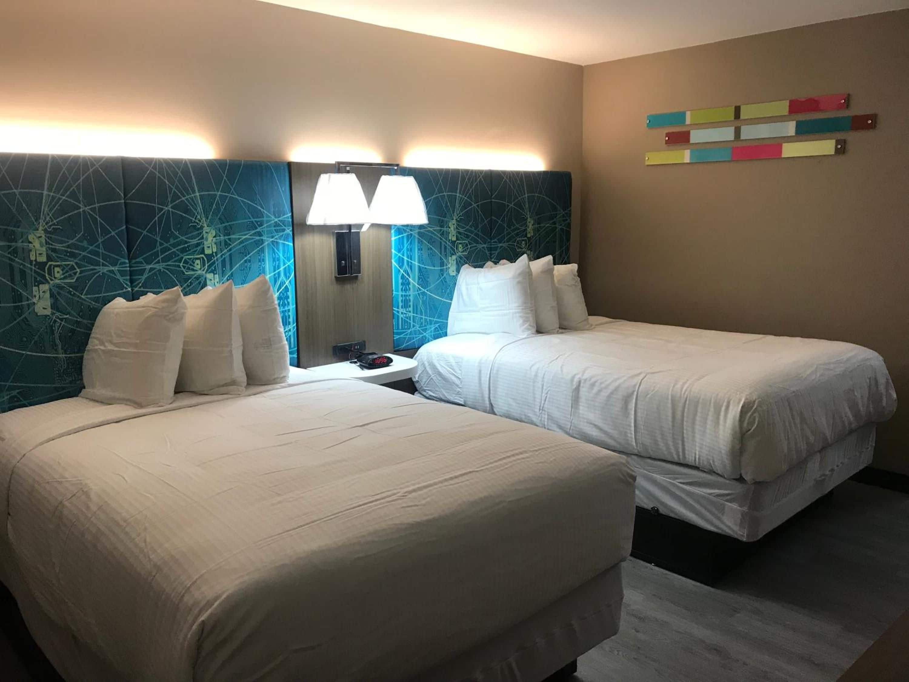 A hotel room with two beds, a nightstand, a lamp, and a wall with colorful horizontal stripes.