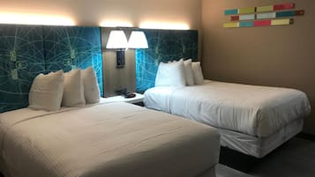 A hotel room with two beds, a nightstand, a lamp, and a wall with colorful horizontal stripes.