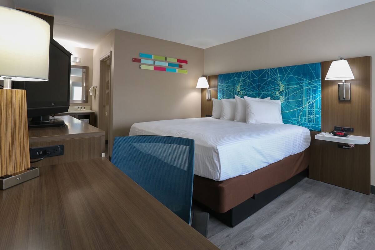 A hotel room with a bed, bedside table, lamp, and a wall art piece.