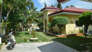 A yellow house with a red roof, surrounded by palm trees and a well-maintained lawn. - Kim Beatriz Compound (Lapu-Lapu)