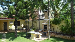 A patio area with a stone barbecue, a stone wall, and a yellow building in the background. - Kim Beatriz Compound (Lapu-Lapu)