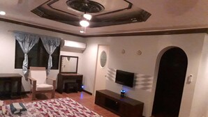 A bedroom with a bed, a chair, a desk, a TV, and a door. - Kim Beatriz Compound (Lapu-Lapu)