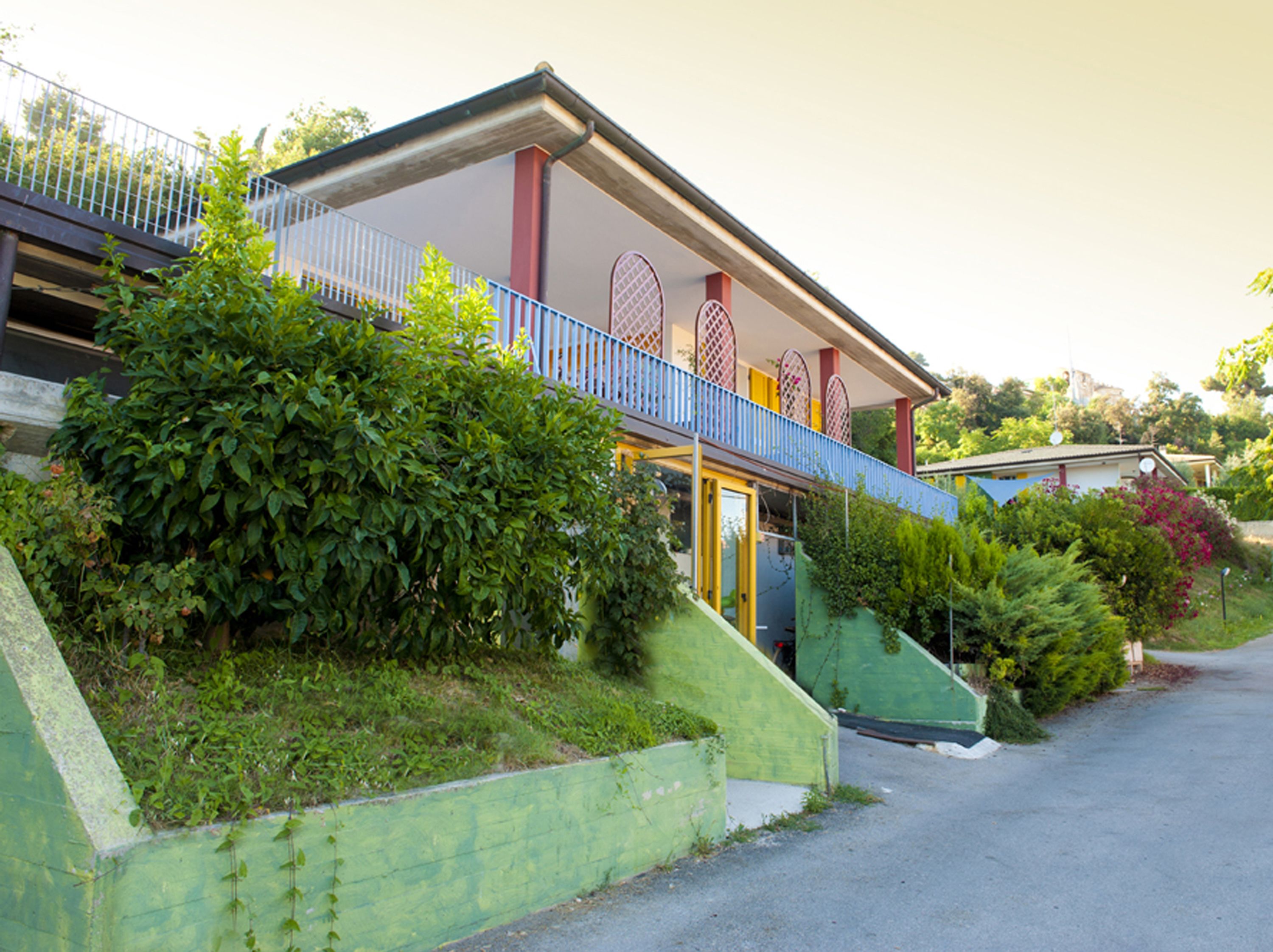 Una casa a due piani con un balcone, immersa nel verde.