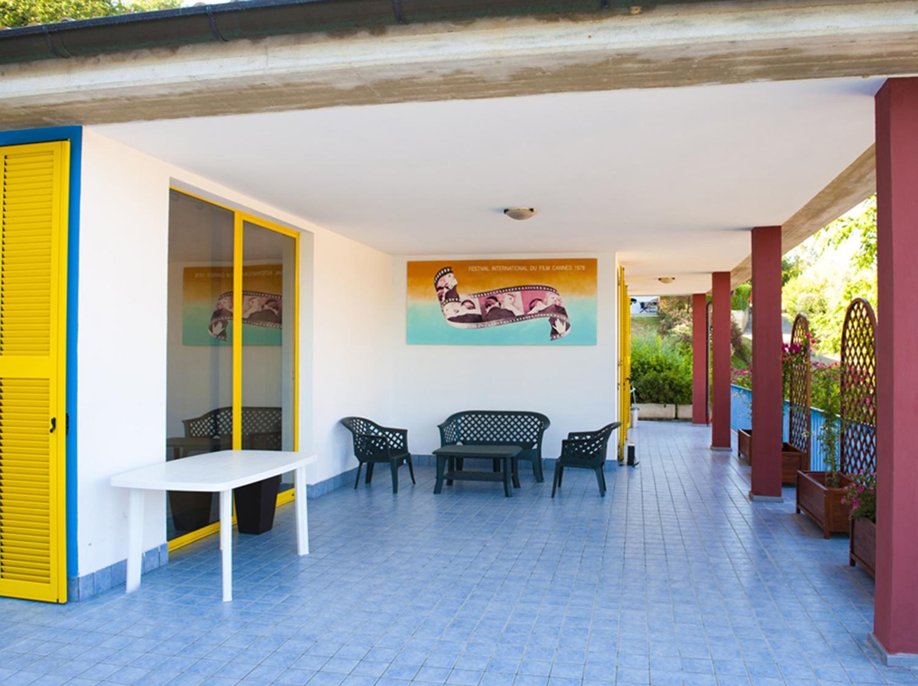 Un patio exterior con una mesa blanca y cuatro sillas, un mural en la pared y un suelo de baldosas.