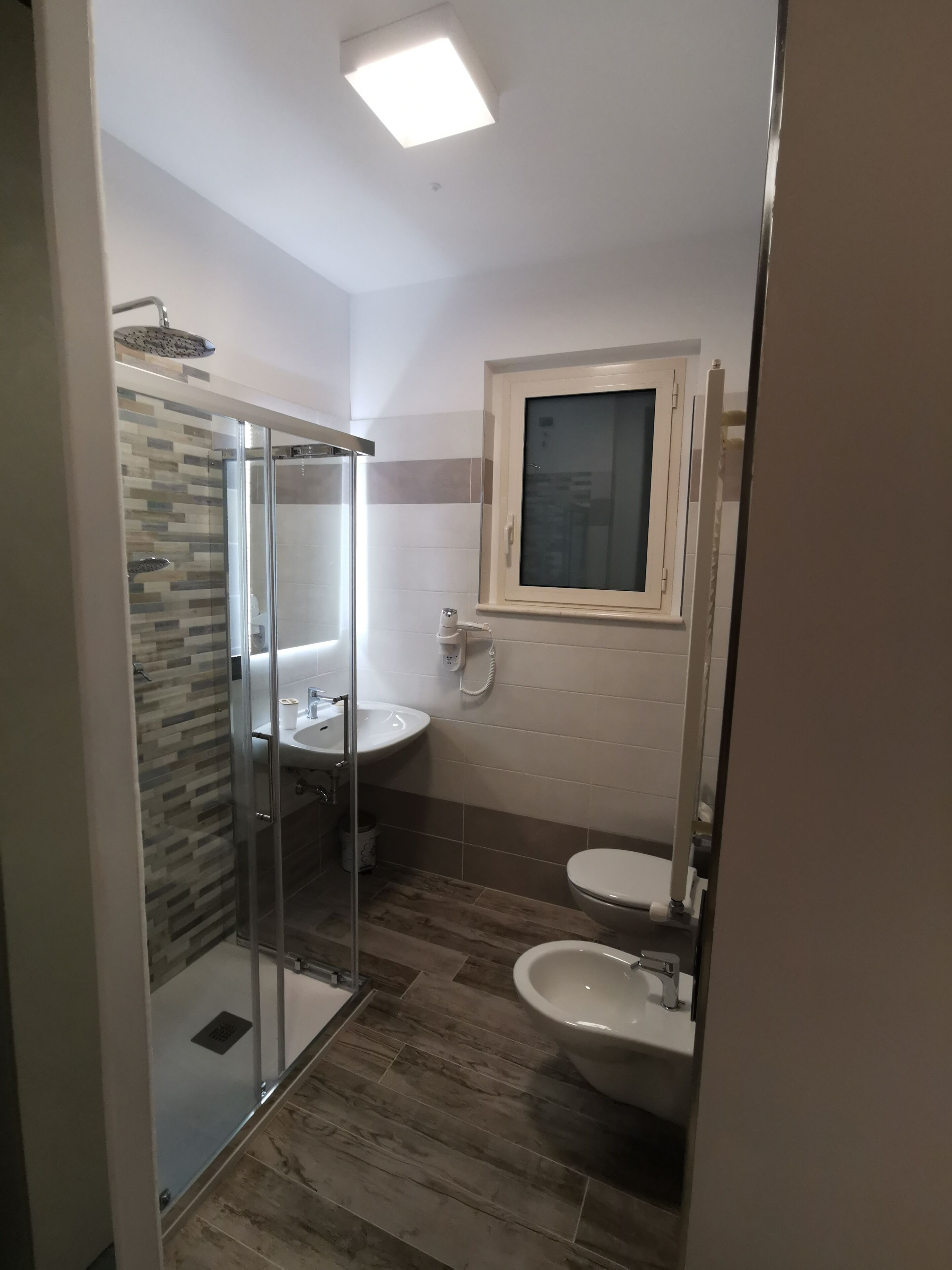 A bathroom with a glass-enclosed shower, a sink, a toilet, and a window above the toilet.