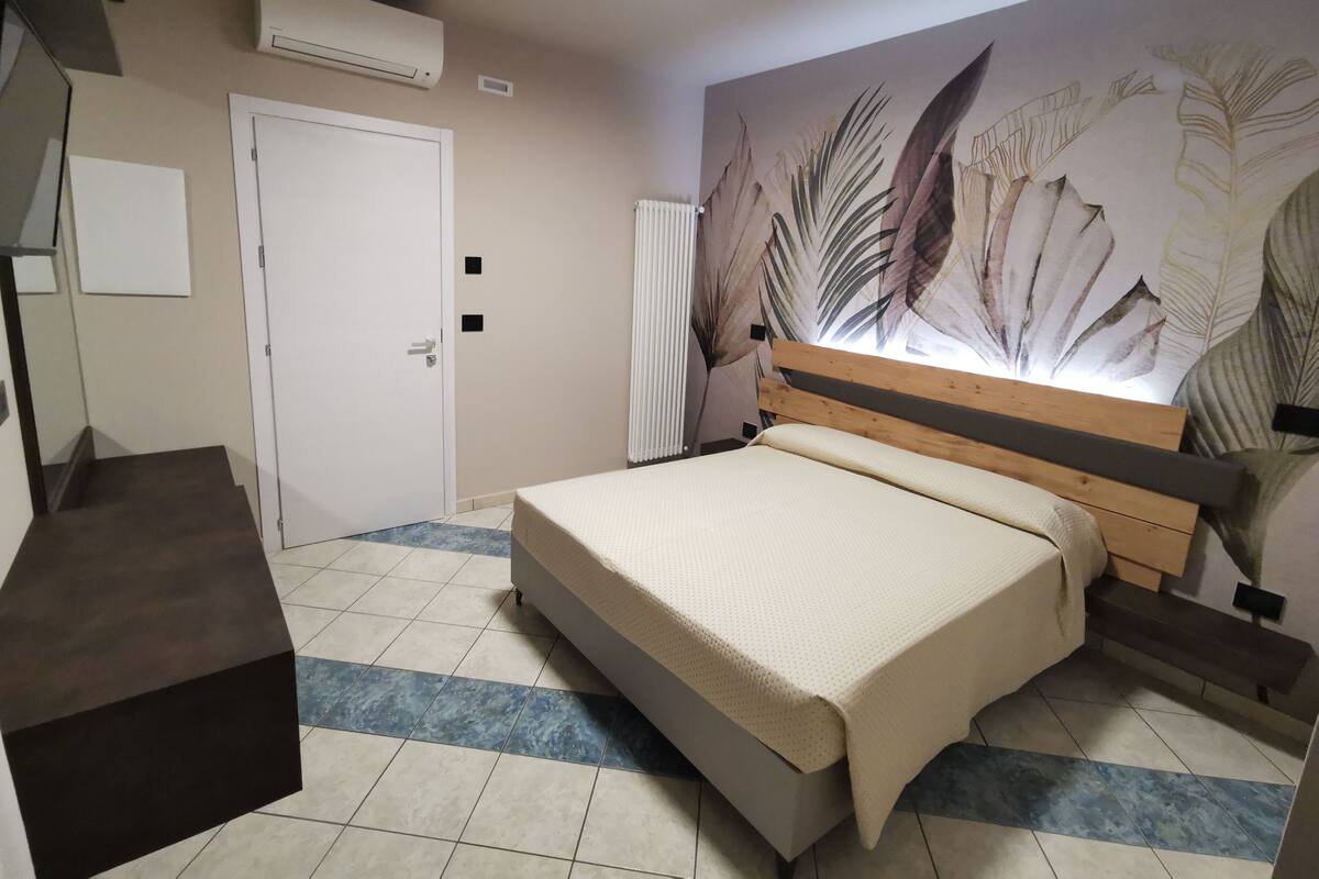 Una camera da letto con un letto, un termosifone, una porta e una parete con motivo a foglia.