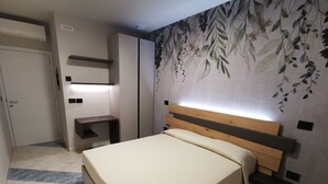Un dormitorio con cama, mesita de noche, estante en la pared y pared con un mural floral.